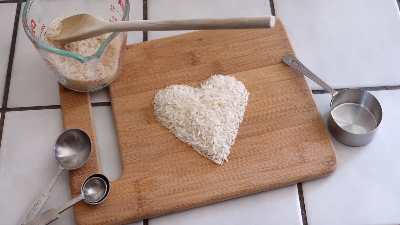 White rice grain animated forming the shape of a heart with cooking utensils and ingredients in a kitchen