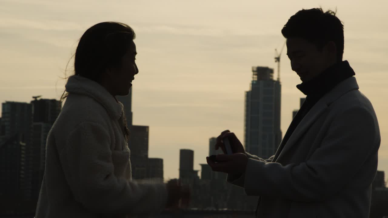 Silhouette Of Couple With Romantic Man Proposing To Woman Against City Skyline