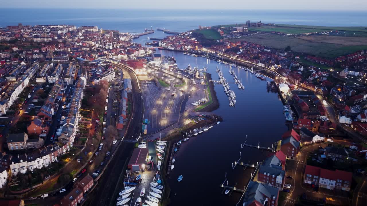 Drone-hyperlapse af Whitby, North Yorkshire, der flyver mod indgangen til havnen med bro i forgrunden, tidlig morgen ved daggry