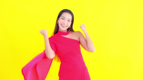 happy asian woman exults in elegant fuchsia dress with yellow screen in background