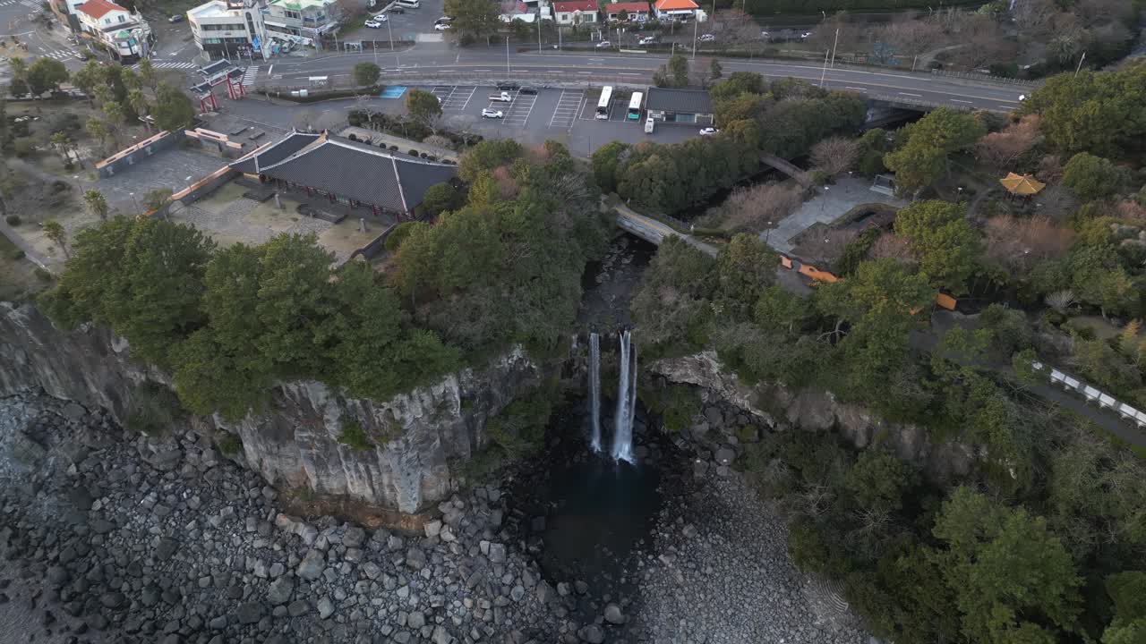 Drone aerial view in South Korea flying in front of a waterfall over the sea rocky area backwards jeju island