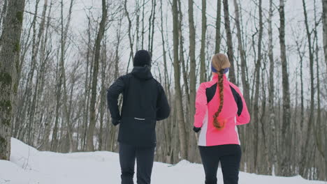 positive beautiful young healthy couple running with sportswear through the forest in the sunny winter morning. the view from the back