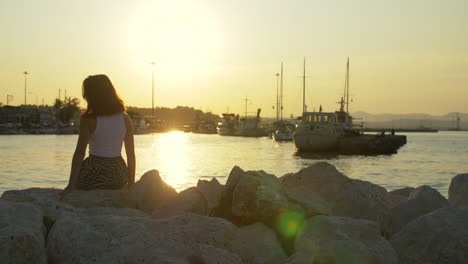 tourist girl on stone at evening sunset in sea port. woman on sunset landscape