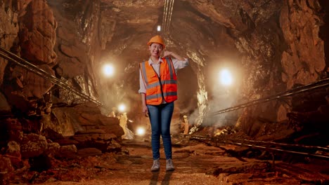 full body of asian female engineer with safety helmet smiling to camera and making call me gesture in underground mine tunnel