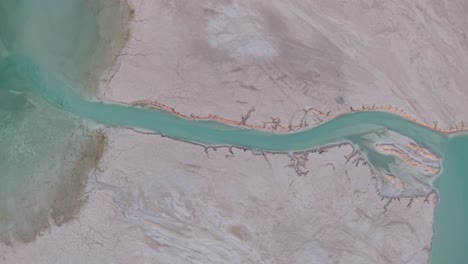 aerial drone view of a turquoise river winding through barren desert terrain with stark contrasts in color