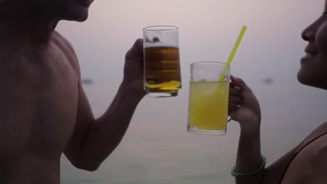 a couple toasting and enjoying drinks by the water at sunset