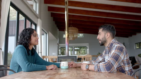 Happy-biracial-couple-sitting-at-table,-drinking-coffee-and-talking-at-home,-in-slow-motion