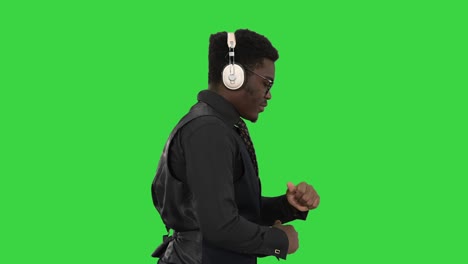 young african american man listening to music in headphones and grooving while walking on a green screen, chroma key