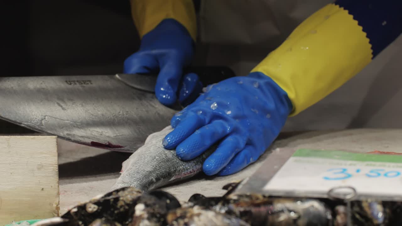 A skilled fishmonger is expertly filleting various fish at a bustling and lively seafood market full of activity