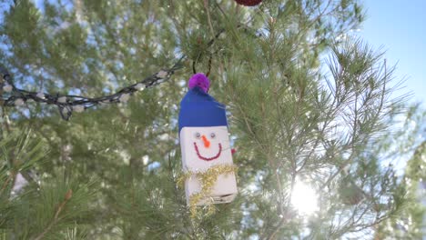 creative handmade snowman ornament hanging among green pine tree branches