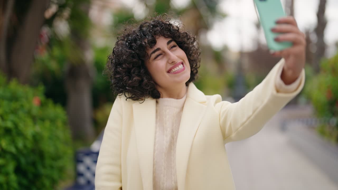 Giovane donna sorridente e fiduciosa che si fa un selfie con lo smartphone al parco.