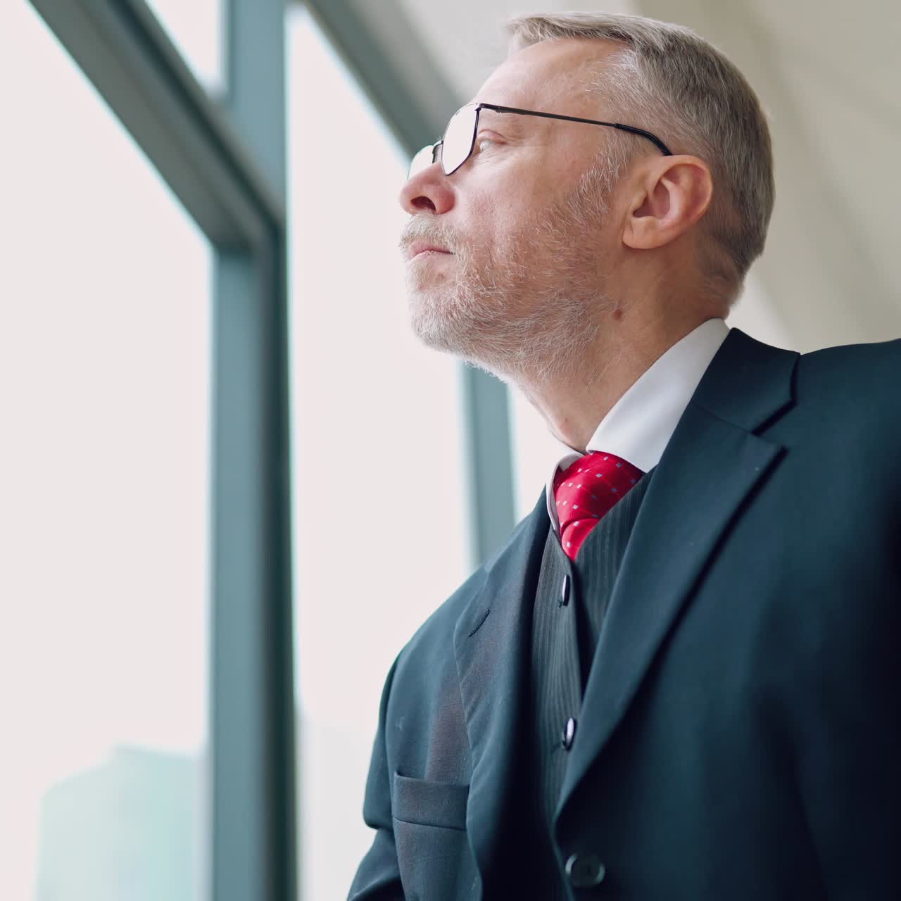 Mature businessman in glasses using laptop. Gray-haired man in costume works with a laptop while sitting at the window in the office.