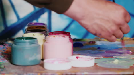 Hand-Painter-Artist-Mixes-Paint-Nearby-Stands-A-Jar-Of-Paint