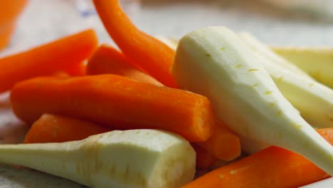 slow moving shot over peeled carrots and parsnips resting on chopping board. naturally lit nutritional organic farmed produce.