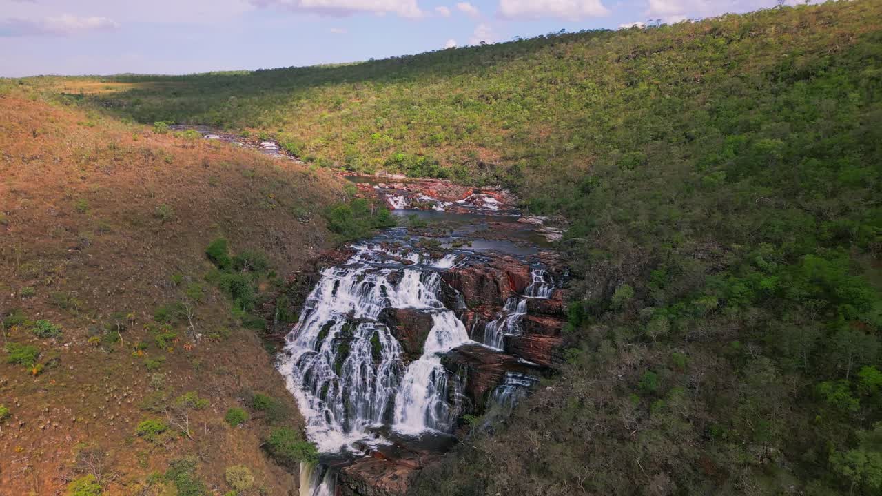 Drone flying forward revealing cataratas dos Couros, a breathtaking waterfall cascading over red rock formations in the lush landscape of Chapada dos Veadeiros national park, Goiás, Brazil