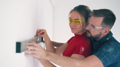 man hugs pretty girl checking level of white wall in room