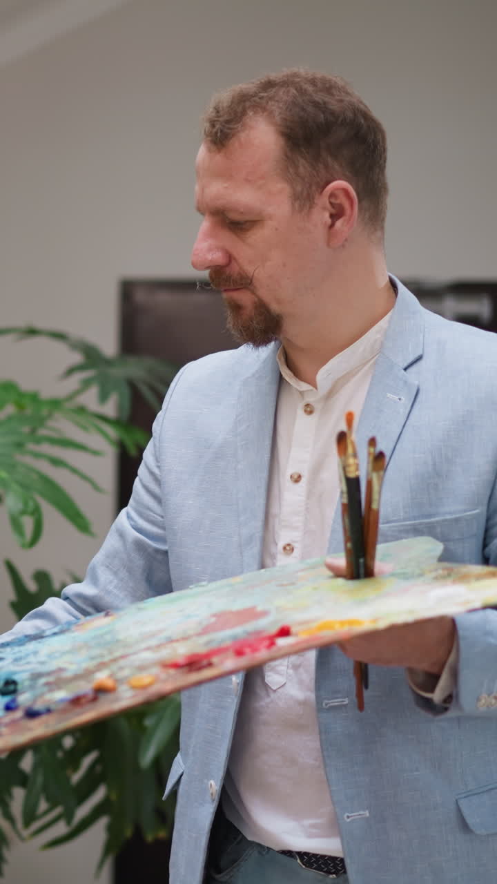 el maestro de arte dibuja en el lienzo en el estudio. un artista elegante en un traje azul elegante crea una imagen sosteniendo la paleta por caballete. un pintor maduro disfruta de la creatividad en la tienda