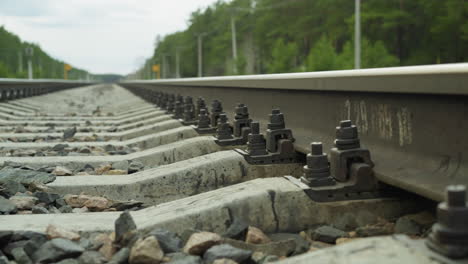 close-up view of railway track fastenings with bolts and nuts securing rails to concrete sleepers, gravel and stones lie between the tracks