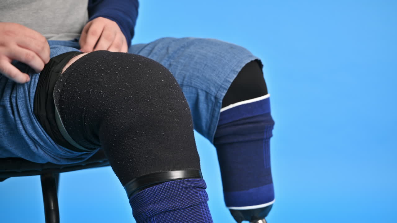 View of a man with prosthetic legs and white sneakers. Putting on the prosthesis while sitting on a chair, blue background