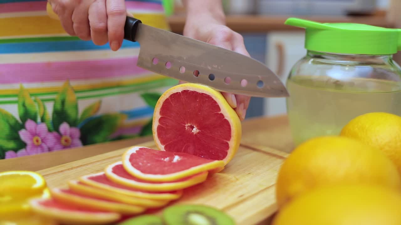 Women's hands Housewives cut with a knife fresh grapefruit on the cutting Board of the kitchen table