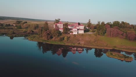 Aerial-pan-drone-shot-of-a-castle-next-to-a-lake-that-reflects-it