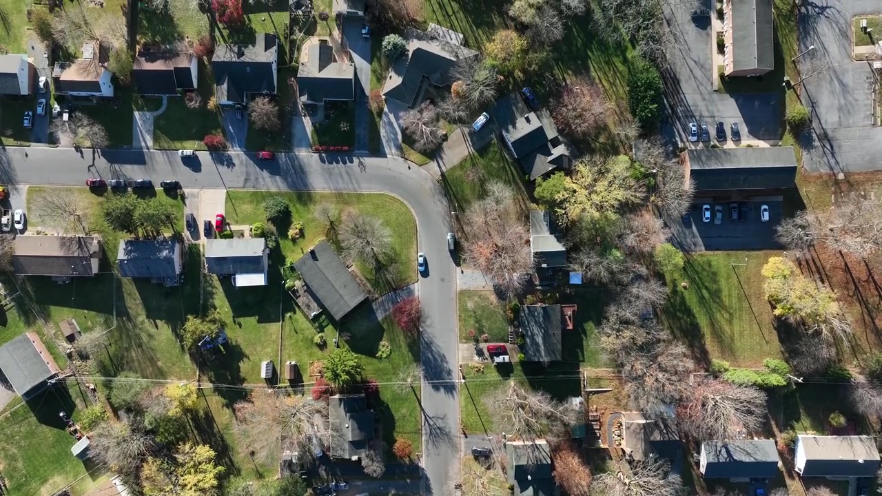 Case unifamiliari con giardino verde in un sobborgo di una piccola città americana. Giornata di sole in autunno. Auto parcheggiate lungo la strada. Ripresa aerea dall'alto con sorvolo.