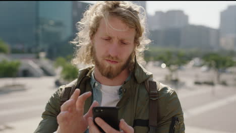portrait of geeky young caucasian man smiling enjoying using smartphone texting browsing social media messages in windy urban city background