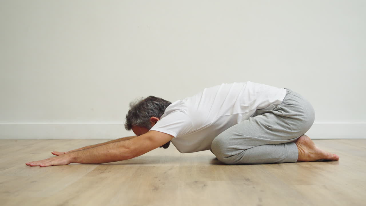 Man Practicing Child's Pose Yoga on Wooden Floor