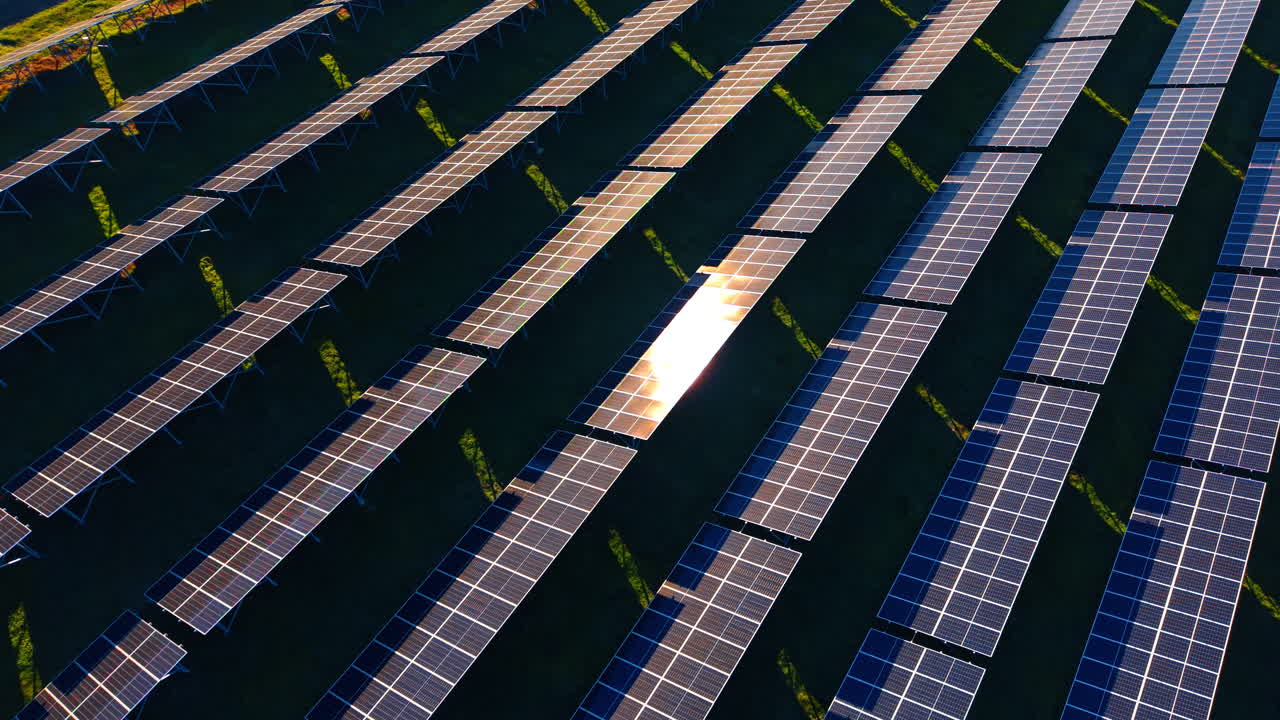Pannelli fotovoltaici in file durante il tramonto con lunghe ombre. Veduta dall'alto di moduli solari installati su un pendio durante l'ora d'oro con luce calda e lunghe ombre.