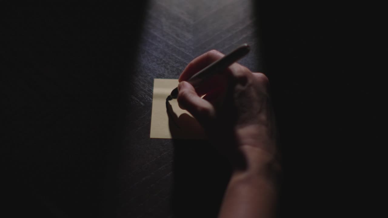 Slow motion close up footage of a hand drawing a heart on a paper note and placing it on a table. Shot in dramatic lighting for an impressive title or transition