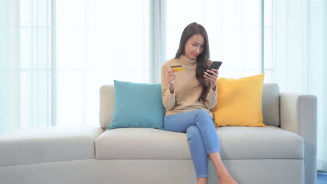 Exulting-Asian-woman-shopping-online-with-credit-card-and-mobile-phone