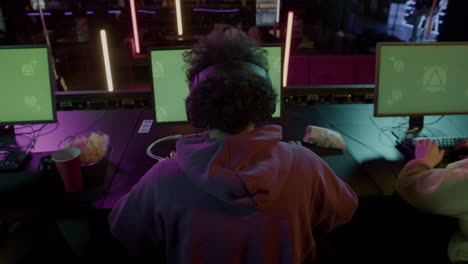 rear view of an gamer playing virtual video games on professional computer with green screen display and raising hands to celebrate victory