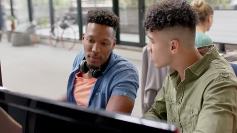 Two-happy-diverse-male-casual-business-colleagues-in-discussion-at-computer-in-office,-slow-motion