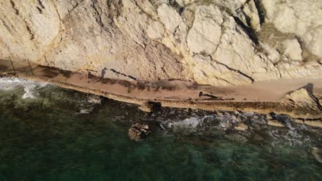 aerial shot orbit in the coast of beska with a woman walking next to adriatic sea and big mountain in a sunny day excelents colors 4k