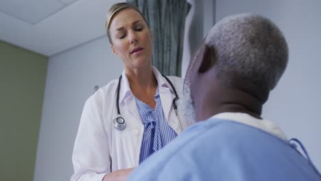 kaukasische ärztin untersucht den hals eines afroamerikanischen älteren männlichen patienten im krankenhaus