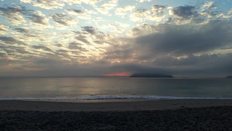몇 개의 구름과 멀리 있는 산이 있는 해변과 그 뒤에 멀리 있는 태양이 떠오르는 해변