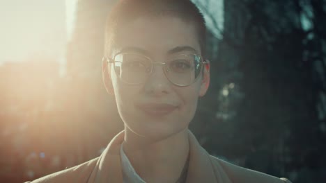 lens flare close-up portrait of happy short haired student woman in eyeglasses smiling at camera outside slow motion.