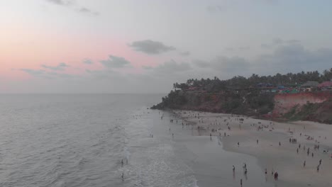 forward moving aerial showing tourists enjoying their holiday on varkala beach during sunset