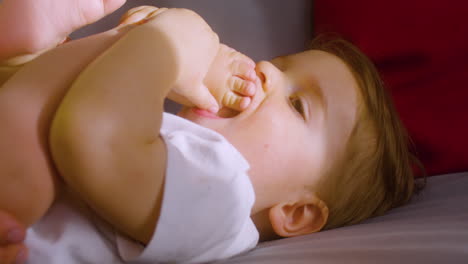 close up view of a smiling baby lying on the sofa at home while his mother tickling and playing with him 1