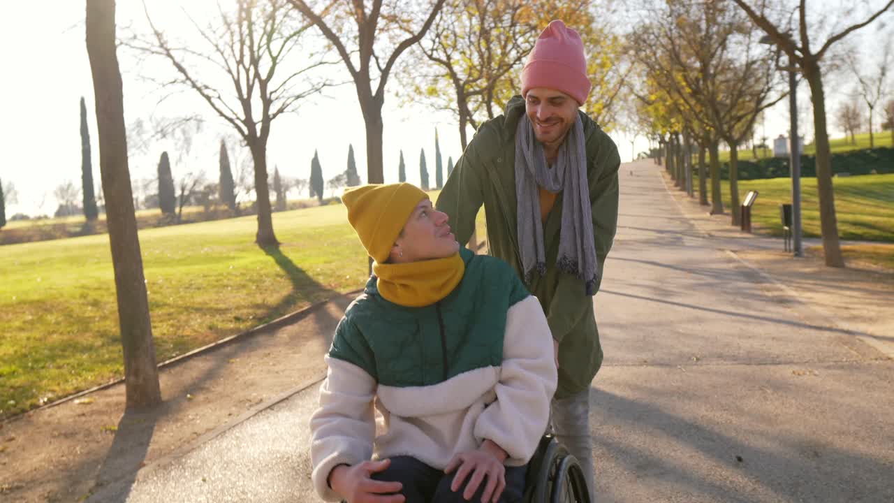 A couple enjoying a sunny day in the park, with one person in a wheelchair being assisted by their partner