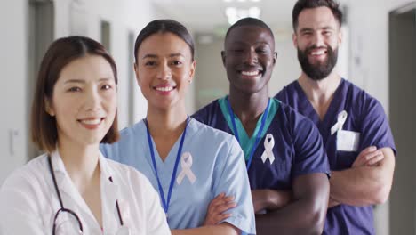 Retrato-En-Video-De-Un-Grupo-Diverso-De-Trabajadores-Médicos-Sonrientes-Con-Cintas-Contra-El-Cáncer-En-El-Pasillo-Del-Hospital