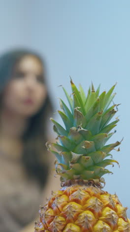 fresh pineapple with bright green top against blurred relaxed women sitting and eating grapes extreme close view