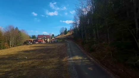 Drone-shot-following-a-country-road-surrounded-by-green-forest-close-to-a-local-house-in-Colibita,-Transilvania,-Romania-Carpathian-area