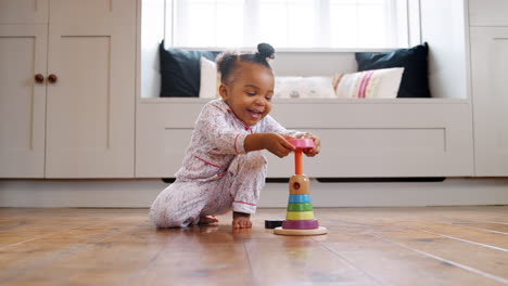 smiling female toddler at home playing with wooden stacking toy