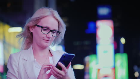 una mujer joven usa un teléfono inteligente en el contexto de las luces publicitarias de los tiempos famosos s