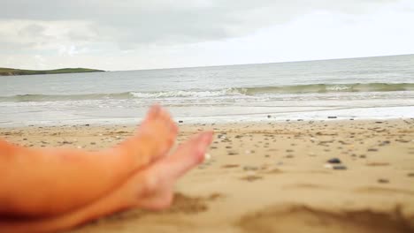 las piernas de la mujer sentadas en la playa junto al agua