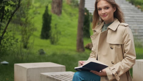 caucasian female student looking at the camera and writing in notebook.