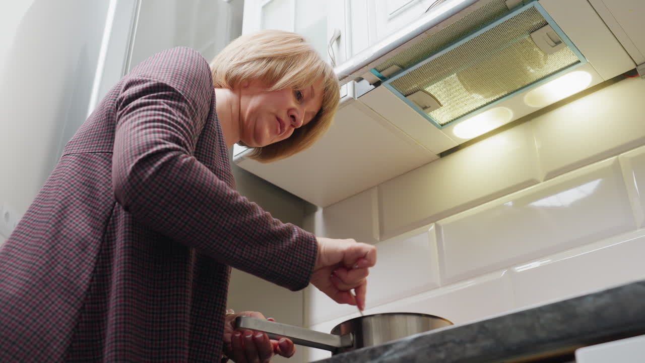 아름다운 현대 주방에서 요리하는 여성의 상단 각도 뷰, 비에 재료를 고, 체크 된 셔츠를 입고, 요리를 즐기고, 배경에 보이는 주방 장비