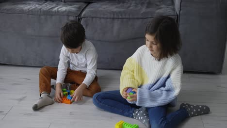 busy little children boy girl siblings friends play brick toy constructor on floor