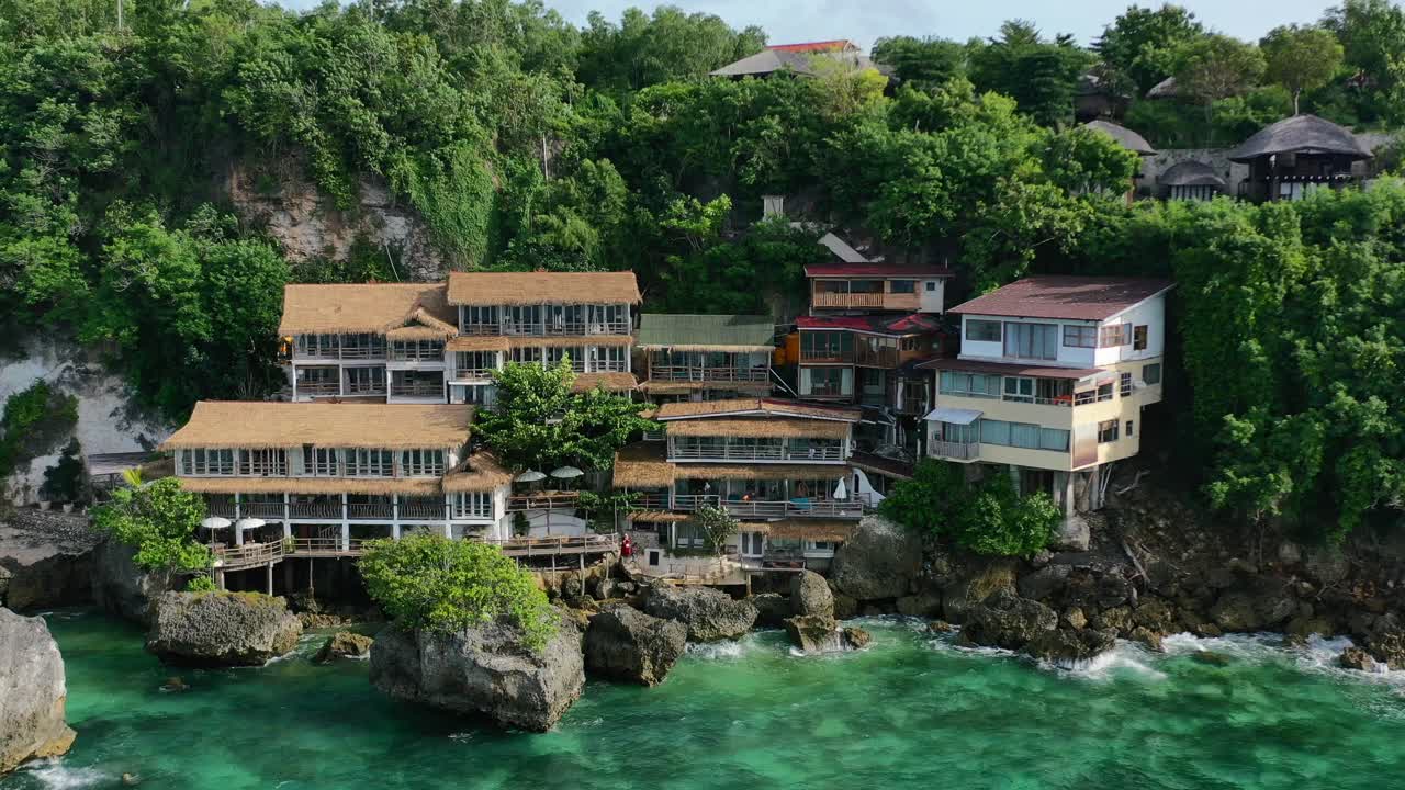 มุมมองทางอากาศแบบซูมออกของโรงแรมริมน้ำเขตร้อนบนหน้าผาในอูลูวาตู บาหลี พร้อมมหาสมุทรสีฟ้าคราม